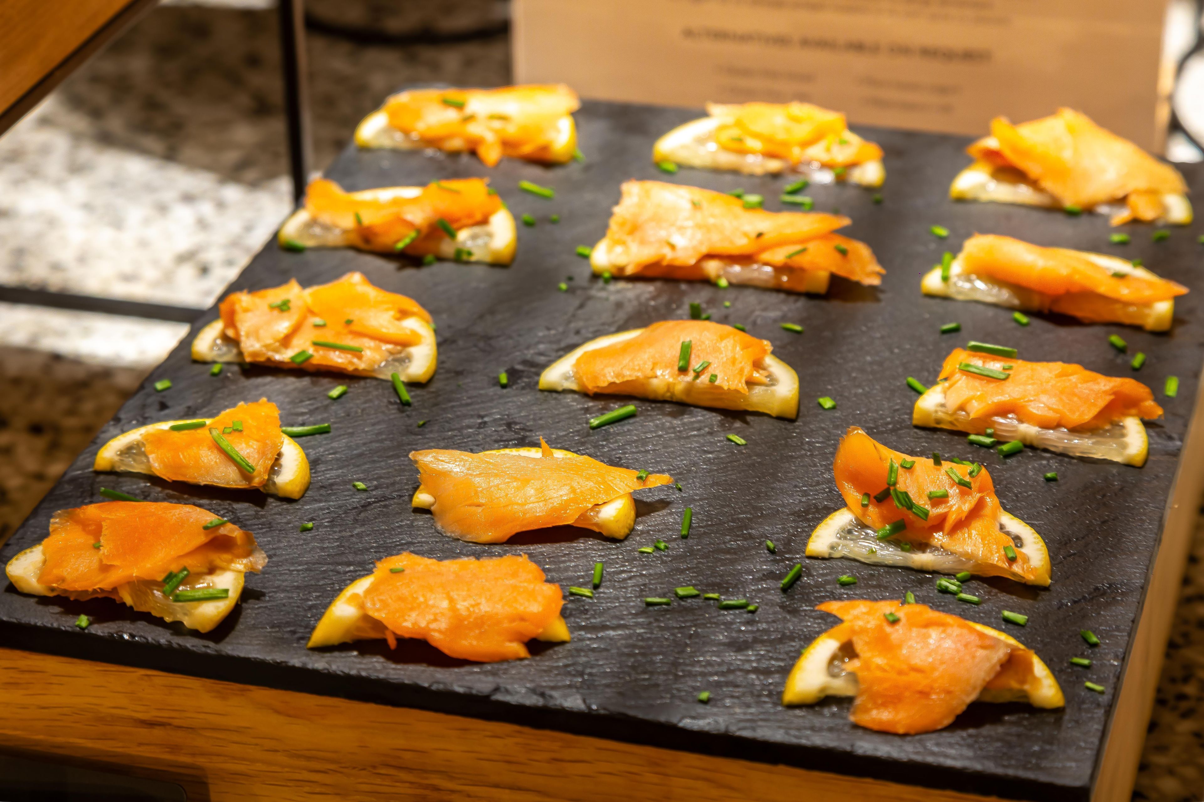 Una tabla de pizarra con aperitivos de salmón adornados con cebollín.