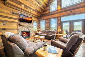 A cozy living room with leather sofas, a fireplace, and a television mounted on a stone wall. - The Lodge at Coopers Hawk | Indoor Pool + Game Room & Hot Tub + VIEWS (Sevierville)