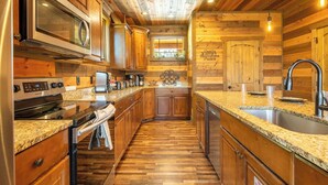 A kitchen with wooden paneling, granite countertops, stainless steel appliances, and a window with a view. - The Lodge at Coopers Hawk | Indoor Pool + Game Room & Hot Tub + VIEWS (Sevierville)