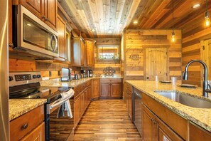 A kitchen with wooden paneling, granite countertops, stainless steel appliances, and a window with a view. - The Lodge at Coopers Hawk | Indoor Pool + Game Room & Hot Tub + VIEWS (Sevierville)