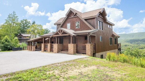 A two-story house with a covered porch, a stone foundation, and a view of a hilly landscape. - The Lodge at Coopers Hawk | Indoor Pool + Game Room & Hot Tub + VIEWS (Sevierville)