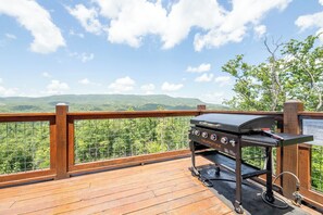 Una parrilla en una terraza de madera con vistas a un paisaje boscoso.