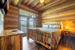 A wooden cabin room with a bed, a small table, and a TV mounted on the wall. - The Lodge at Coopers Hawk | Indoor Pool + Game Room & Hot Tub + VIEWS (Sevierville)