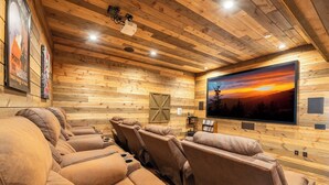 A home theater with wooden paneling, reclining leather seats, and a large flat-screen TV displaying a sunset. - The Lodge at Coopers Hawk | Indoor Pool + Game Room & Hot Tub + VIEWS (Sevierville)