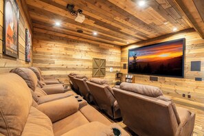 A home theater with wooden paneling, reclining leather seats, and a large flat-screen TV displaying a sunset. - The Lodge at Coopers Hawk | Indoor Pool + Game Room & Hot Tub + VIEWS (Sevierville)
