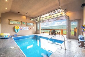 En inomhuspool med utsikt över landskapet, en livräddarstation och ett område med sittplatser vid poolkanten.