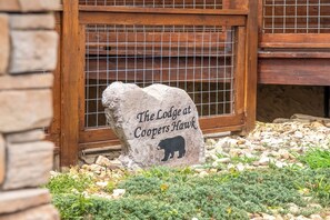 A stone sign with a bear silhouette and text, set against a wooden structure with a metal grid window. - The Lodge at Coopers Hawk | Indoor Pool + Game Room & Hot Tub + VIEWS (Sevierville)