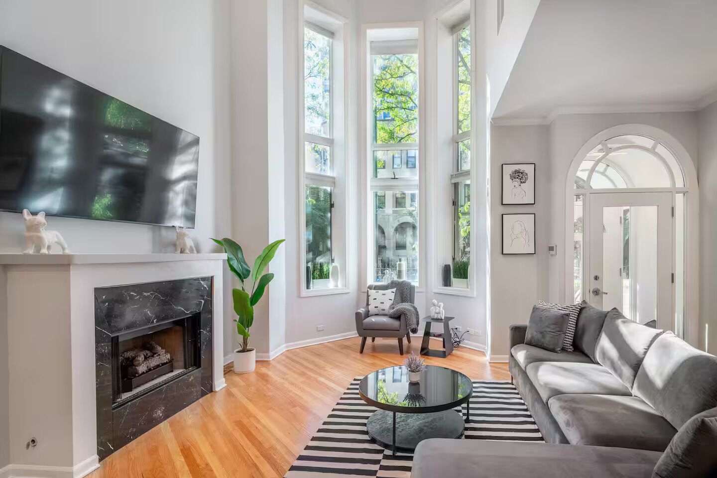 A modern living room with a fireplace, a flat-screen TV, a sofa, a coffee table, and large windows.