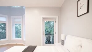 A bedroom with a bed, a bedside table, a lamp, a framed picture on the wall, and a door leading to a balcony. - Gold Coast Home - Rooftop - PoolTable - Parking - Views (Chicago)