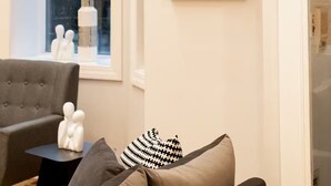 A room with a large window, a grey sofa, two framed line art pieces on the wall, and a small black side table with decorative items. - Gold Coast Home - Rooftop - PoolTable - Parking - Views (Chicago)