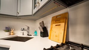 A kitchen with a white countertop, a sink, a stove, and a wooden cutting board. - Pristine Gold Coast 3BD - 2BA - Free Parking - Beach. (Chicago)