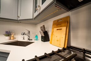 Une cuisine avec un plan de travail blanc, un évier, une cuisinière et une planche à découper en bois.
