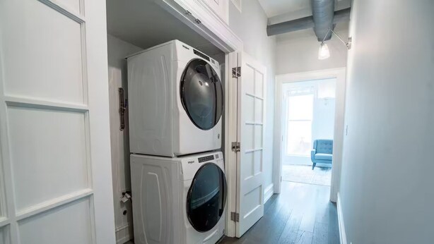 A laundry room with stacked front-loading washers and dryers, a hallway leading to a living area with a blue chair. - Pristine Gold Coast 3BD - 2BA - Free Parking - Beach. (Chicago)