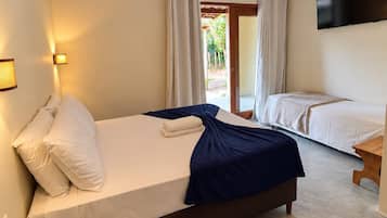 Quarto de hotel com cama grande, mesa de cabeceira, TV de tela plana na parede e vista para o exterior através de uma porta deslizante.