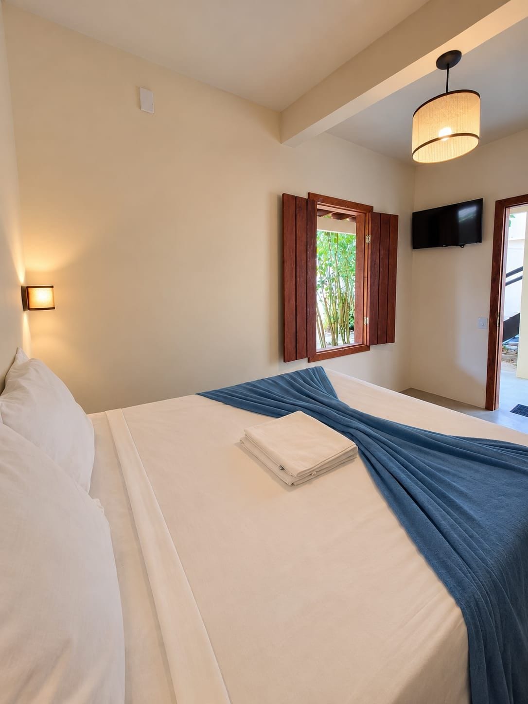 Quarto de hotel com cama, televisão de tela plana na parede e janela com persianas de madeira.