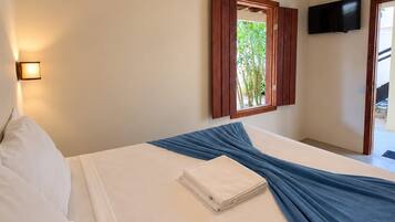 Quarto de hotel com cama, televisão de tela plana na parede e janela com persianas de madeira.