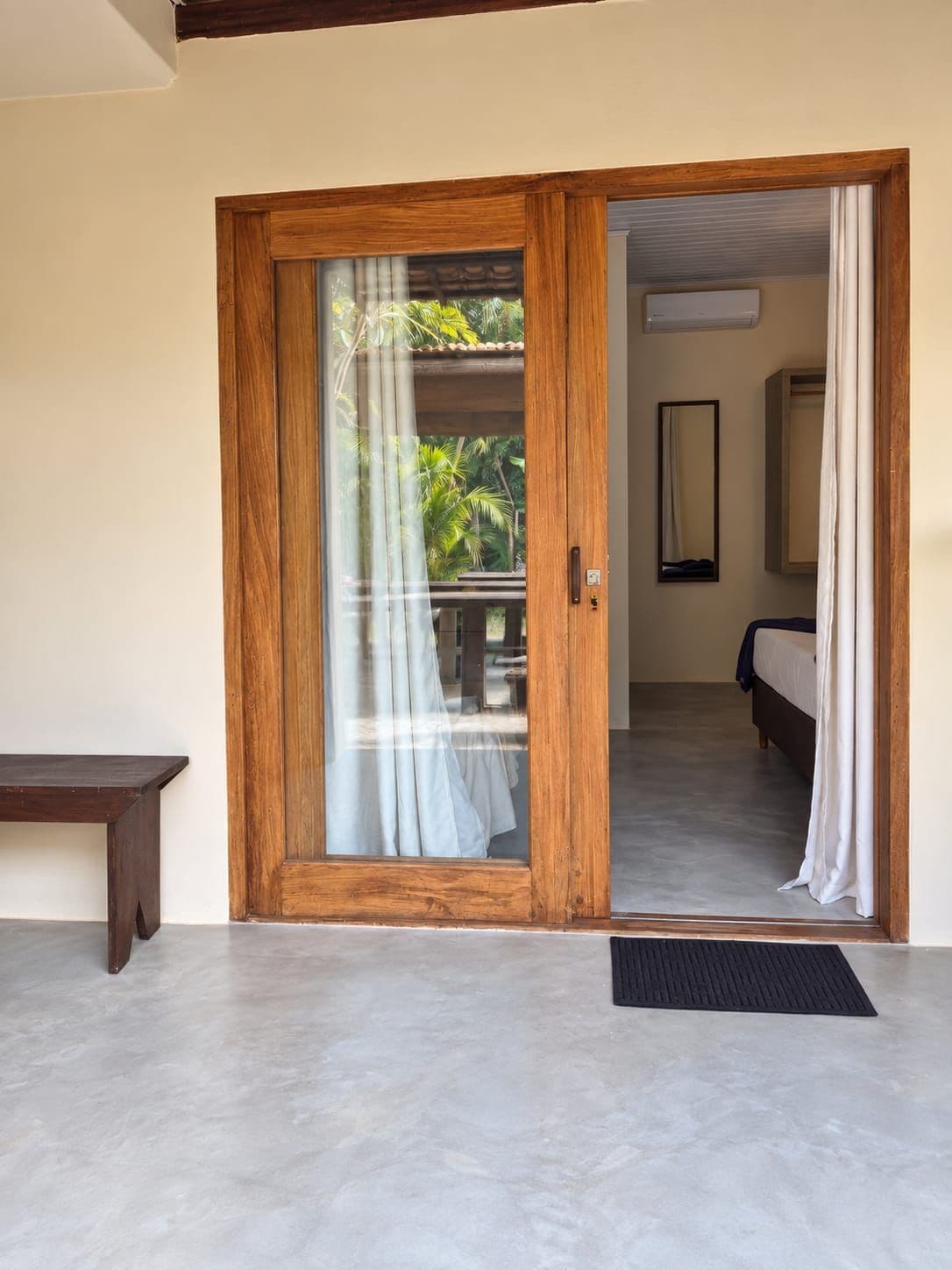 Quarto com porta de madeira que dá para uma varanda com vista para palmeiras.