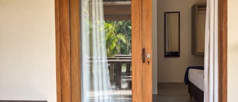 A room with a wooden door leading to a balcony with a view of palm trees.