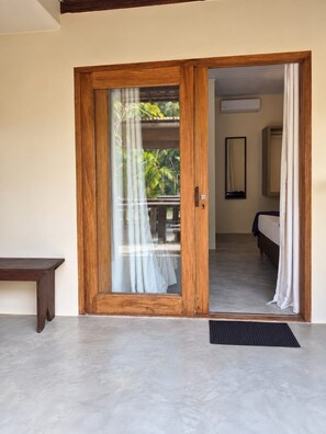 A room with a wooden door leading to a balcony with a view of palm trees.