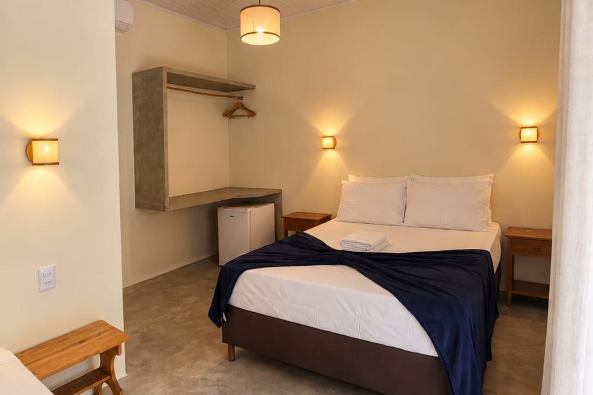A bedroom with a bed, bedside tables, a hanging light fixture, and a small desk with a chair.