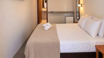 Quarto de hotel com cama, mesa de cabeceira, TV fixada na parede, espelho e luminária no teto.