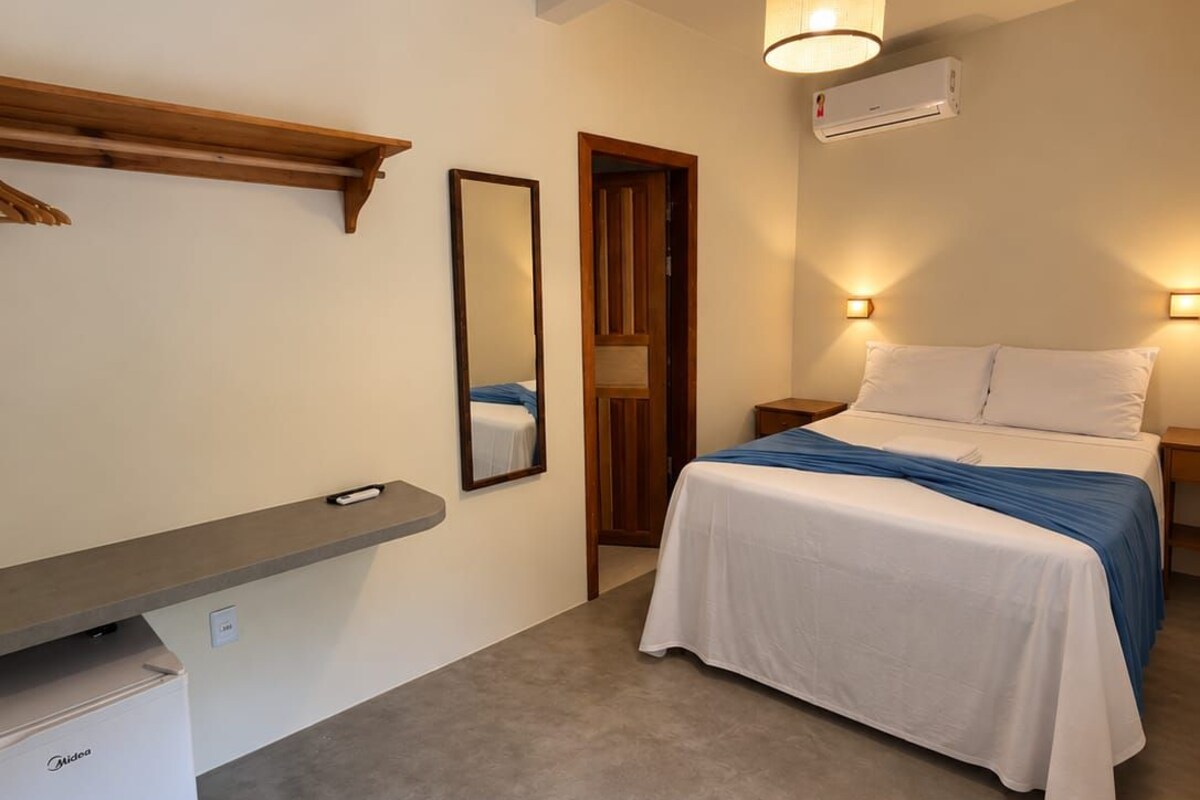 A bedroom with a bed, bedside tables, a mirror, a shelf, and a small refrigerator.