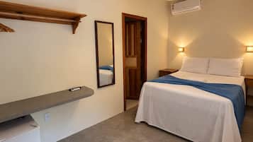 Quarto com cama, mesas de cabeceira, espelho, prateleira e um pequeno frigorífico.