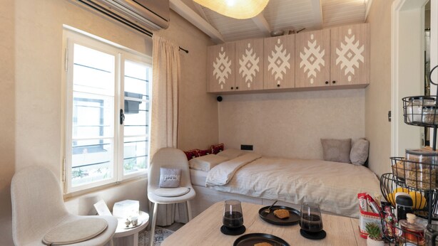 A bedroom with a bed, a chair, a table with plates and glasses, and a window with curtains. - Authentic Bosnian-Herzegovinian Studio & Garden in the heart of Mostar (Mostar)