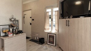 A hotel room with a wooden cabinet, a TV, a window with curtains, a framed picture, and a small shelf with items. - Authentic Bosnian-Herzegovinian Studio & Garden in the heart of Mostar (Mostar)