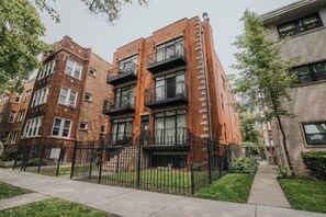 Un immeuble d’appartements à plusieurs étages, avec des façades en briques, des balcons et une entrée fermée par un portail.