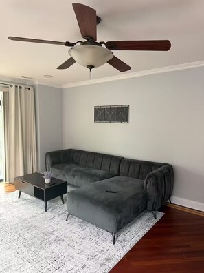 Ein Wohnzimmer mit Ecksofa, Couchtisch, Deckenventilator und einer Wanddekoration.