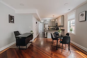 Una cocina moderna con armarios blancos, un comedor con mesa y sillas negras, y un pasillo que conduce a una sala de estar.
