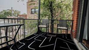 Ein Balkon mit dunklem, gemustertem Boden, zwei Korbstühlen und einem Tisch.