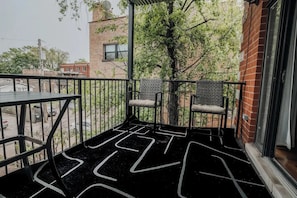 Un balcón con piso estampado negro, dos sillas de mimbre y una mesa.