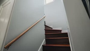 Eine Treppe mit hölzernen Geländern und weißen Stufen, die zu einem Zwischenpodest mit einem Fenster führt.