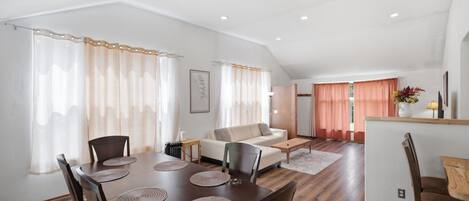 A spacious living area with a dining table, chairs, a sofa, and a kitchen area with a countertop.
