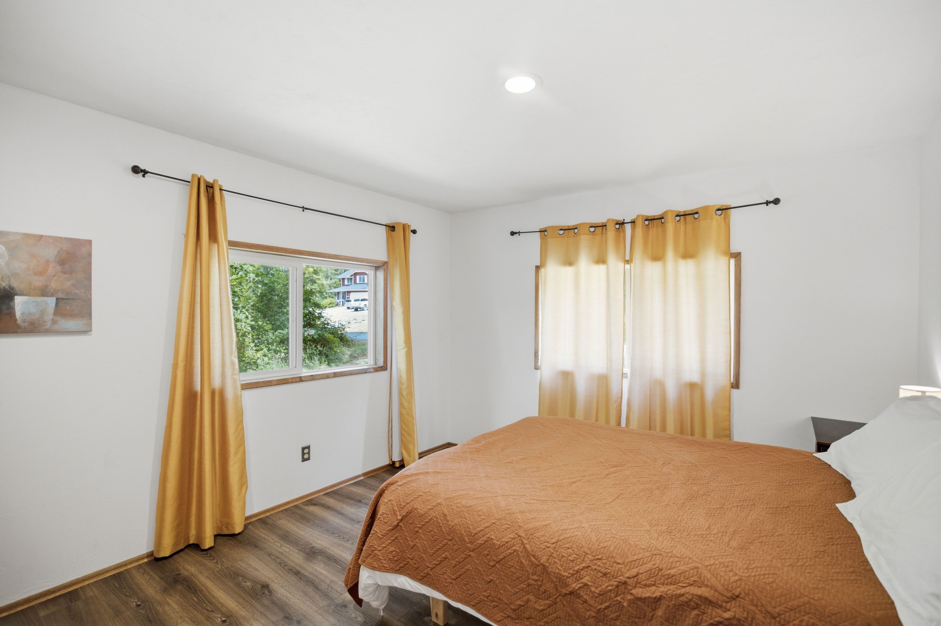 A bedroom with a bed, curtains, a window, and a painting on the wall.