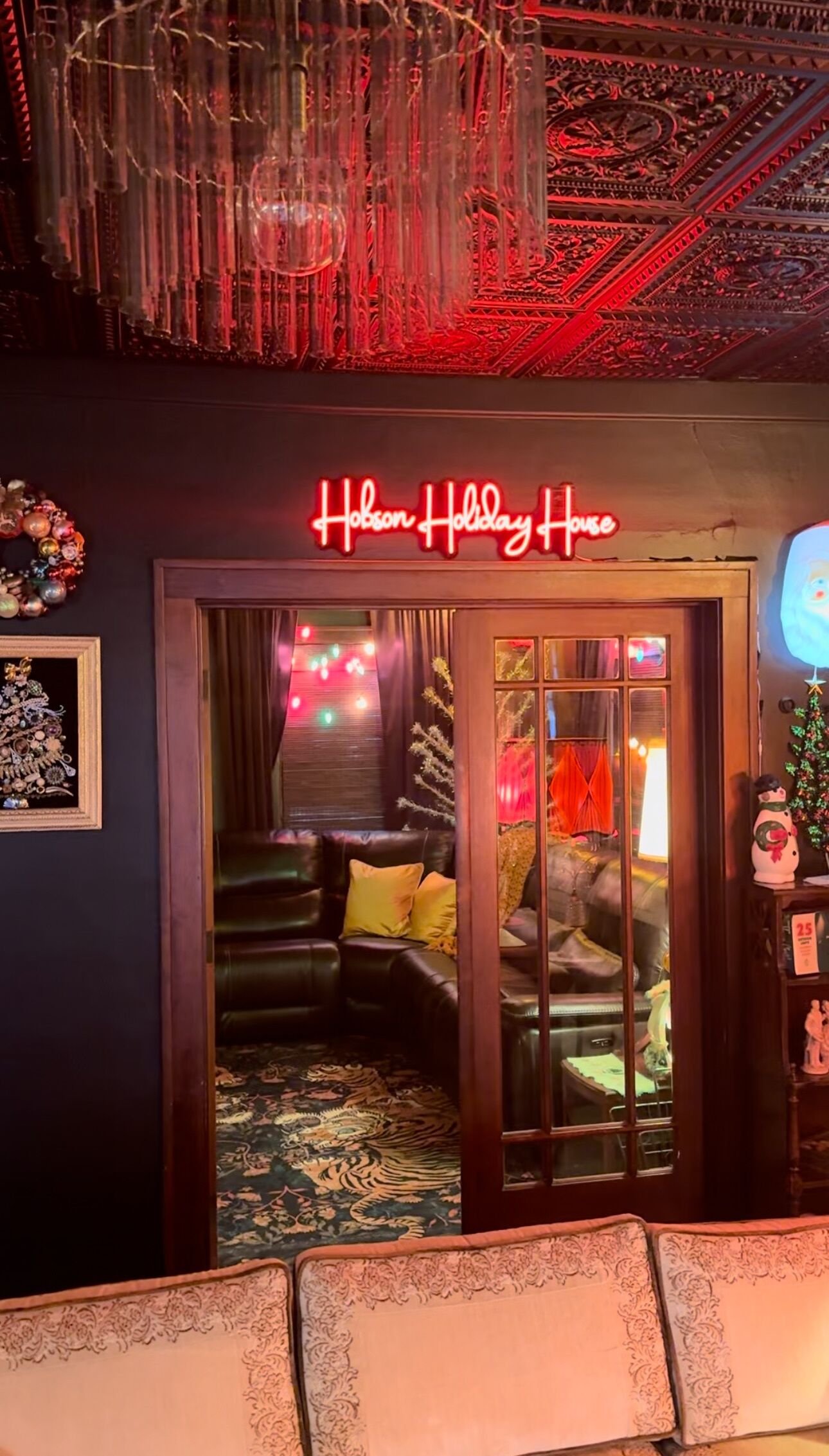 En hyggelig indretning med et neonlys, der viser 'Hobson Holiday House', en lædersofa og en tæppe med et mønster.