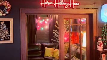 En hyggelig indretning med et neonlys, der viser 'Hobson Holiday House', en lædersofa og en tæppe med et mønster.