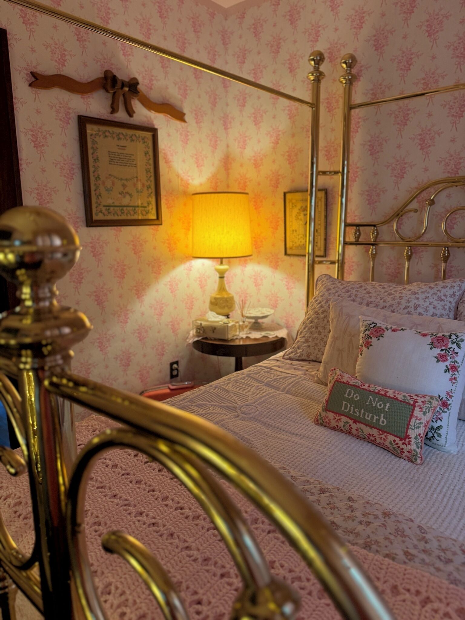 Een slaapkamer met een bed, nachtkastje, lamp, een bed met bronzen frame en bloemenbehang.