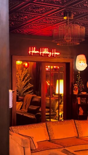 Un hall de hotel con un letrero de neón que dice 'Holiday House', un árbol de Navidad y una zona de estar con sofás.