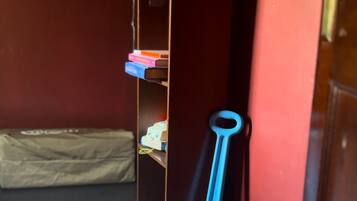 Ein Zimmer mit einem weißen, flauschigen Teppich, einem Holzregal mit Büchern, einem blauen Spielzeug und einer roten Tür.