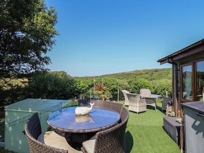 Um pátio com móveis de vime, uma mesa redonda e vista para uma paisagem verde.