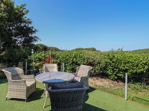 A patio with wicker furniture, a round table, and a view of a vineyard. - Excalabur 10 (Porthmadog)