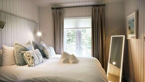 En pænt redt seng med puder, en sengetavlelampe, et spejl og et vindue med gardiner.