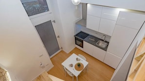 Une cuisine compacte avec des meubles blancs, une petite table à manger avec des chaises et une fenêtre donnant sur un jardin.