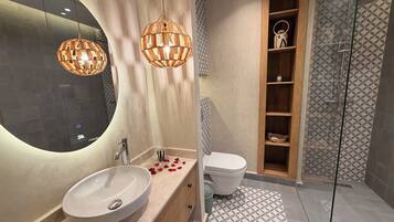 Ein Badezimmer mit rundem Spiegel, Waschbecken in Weiß, Toilette und Duschbereich.