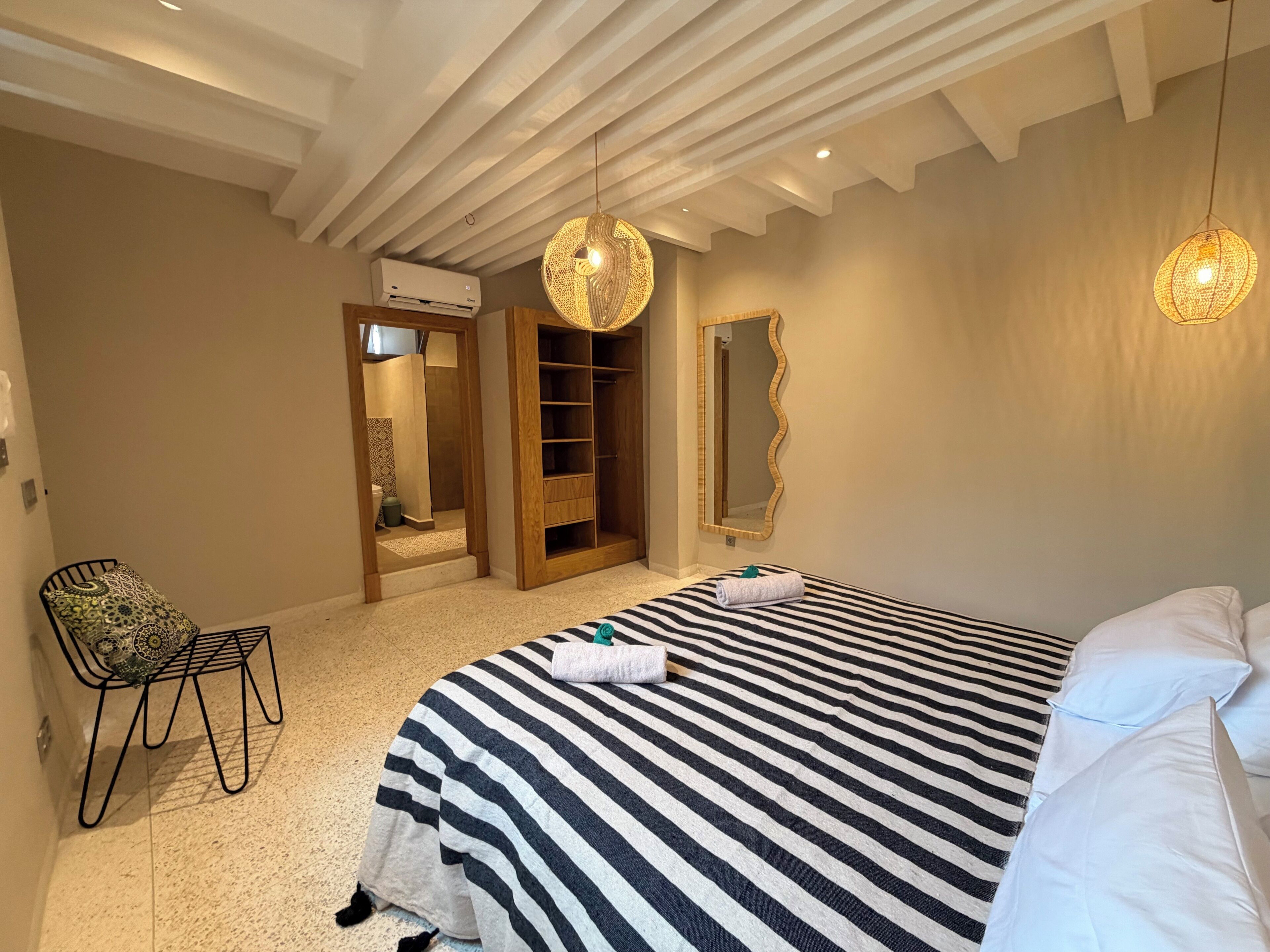 A bedroom with a striped bedspread, a chair, a wardrobe, and a mirror.