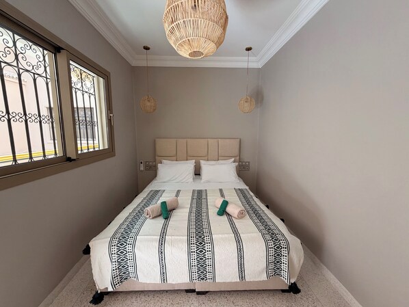 Een slaapkamer met een bed, twee bedlampen, een raam met metalen tralies en een plafondlamp.