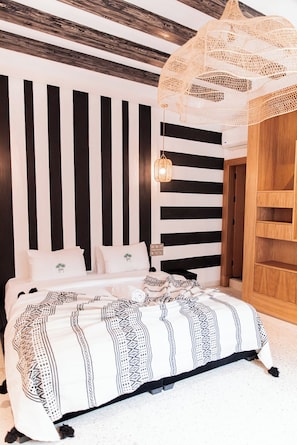 A bedroom with a bed, a hanging light fixture, and a wooden wardrobe. - riad 16 art (Marrakech)